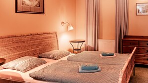 Une chambre à coucher avec un lit, une table de chevet, une lampe, une commode et une fenêtre avec des rideaux.