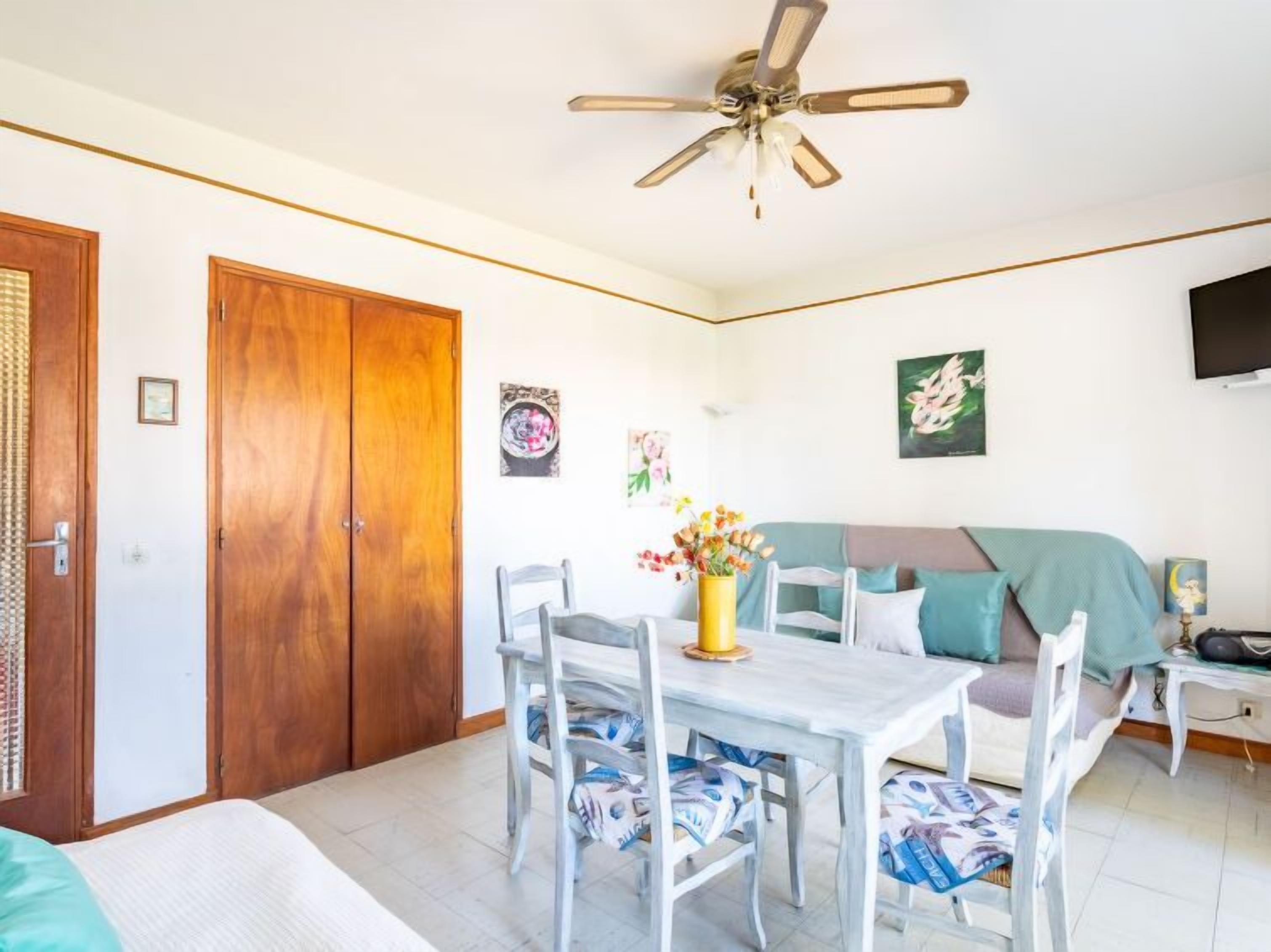 A room with a dining table, chairs, a sofa, a ceiling fan, and artwork on the walls.