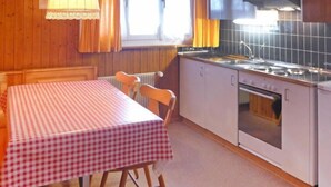 Een keuken met een geruit tafelkleed, houten stoelen, een fornuis en een raam met gordijnen.