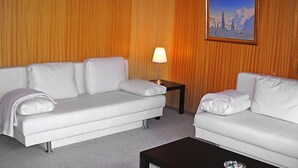 Een hotelkamer met twee witte banken, een kleine tafel met een lamp en een ingelijst schilderij aan de muur.