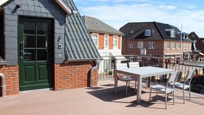 Un balcon avec une table et des chaises, une porte verte et un mur en briques.