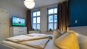 Une chambre à coucher avec un lit, une télévision, une commode et une fenêtre avec des rideaux.