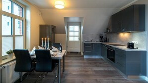 Une cuisine moderne avec des meubles sombres, un coin repas avec une table dressée pour deux personnes, et une vue sur l’extérieur par une fenêtre.