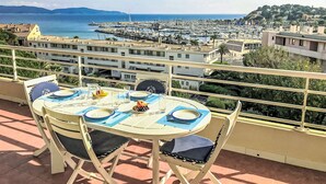 A balcony with a table set for dining, overlooking a marina and coastal town. - Le Grand Pavois by Interhome (Cavalaire)