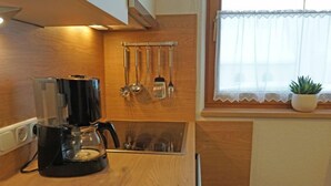 Eine kleine Küche mit Kaffeemaschine, Kochutensilien, die an der Wand hängen, und einem Fenster mit einem Blumentopf.