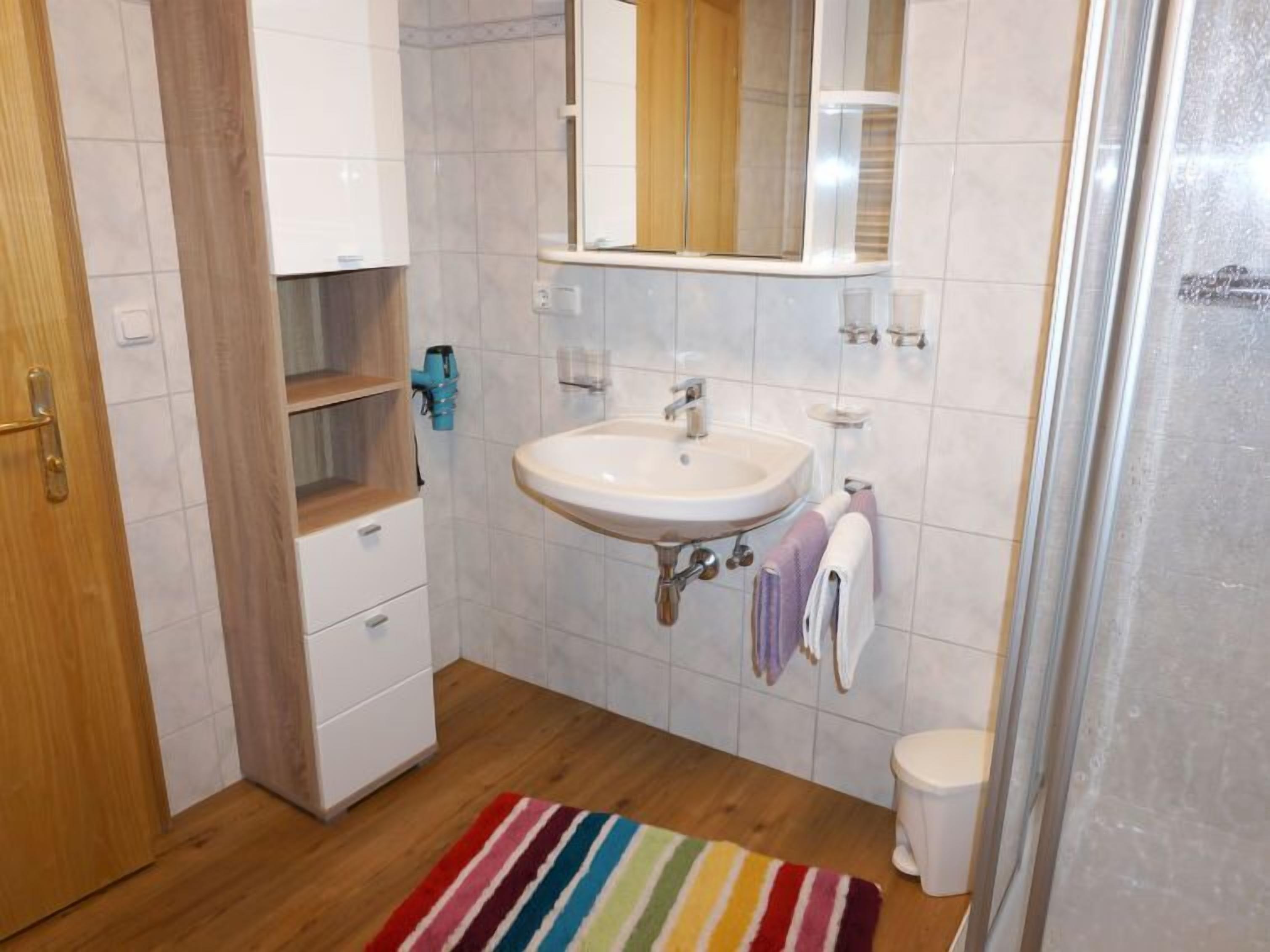 A bathroom with a white sink, wooden cabinets, a mirror, and a striped rug.