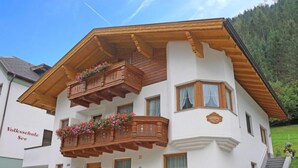Ein zweistöckiges Gebäude mit einem an Blumen bepflanzten Balkon, einem Schild mit der Aufschrift 'Volksschule See' und einer Treppe, die zu der oberen Etage führt.