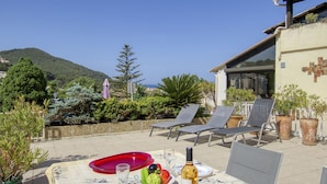 An outdoor dining area with a table set for two, a bottle of wine, and a view of the sea and hills. - La Madrague d'Azur by Interhome (Saint Cyr sur Mer La Madrague)