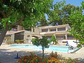 Ein zweigeschossiges Gebäude mit Swimmingpool, umgeben von Grünflächen und Topfpflanzen.