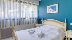 A bedroom with a bed, a nightstand, a lamp, a window with sheer curtains, and a framed picture on the wall. - La Madrague d'Azur by Interhome (Saint Cyr sur Mer La Madrague)