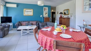 A living room with a blue wall, a sofa, a TV, and a dining table with a red tablecloth. - La Madrague d'Azur by Interhome (Saint Cyr sur Mer La Madrague)