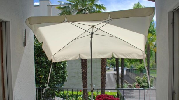 A balcony with a table, chairs, a potted plant, and a large umbrella. - Tre G OG by Interhome (Solduno)