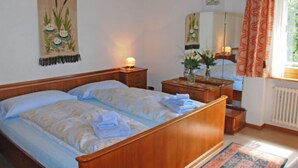 A bedroom with a wooden bed, a nightstand with a lamp, a mirror, and a window with curtains. - Tre G OG by Interhome (Solduno)