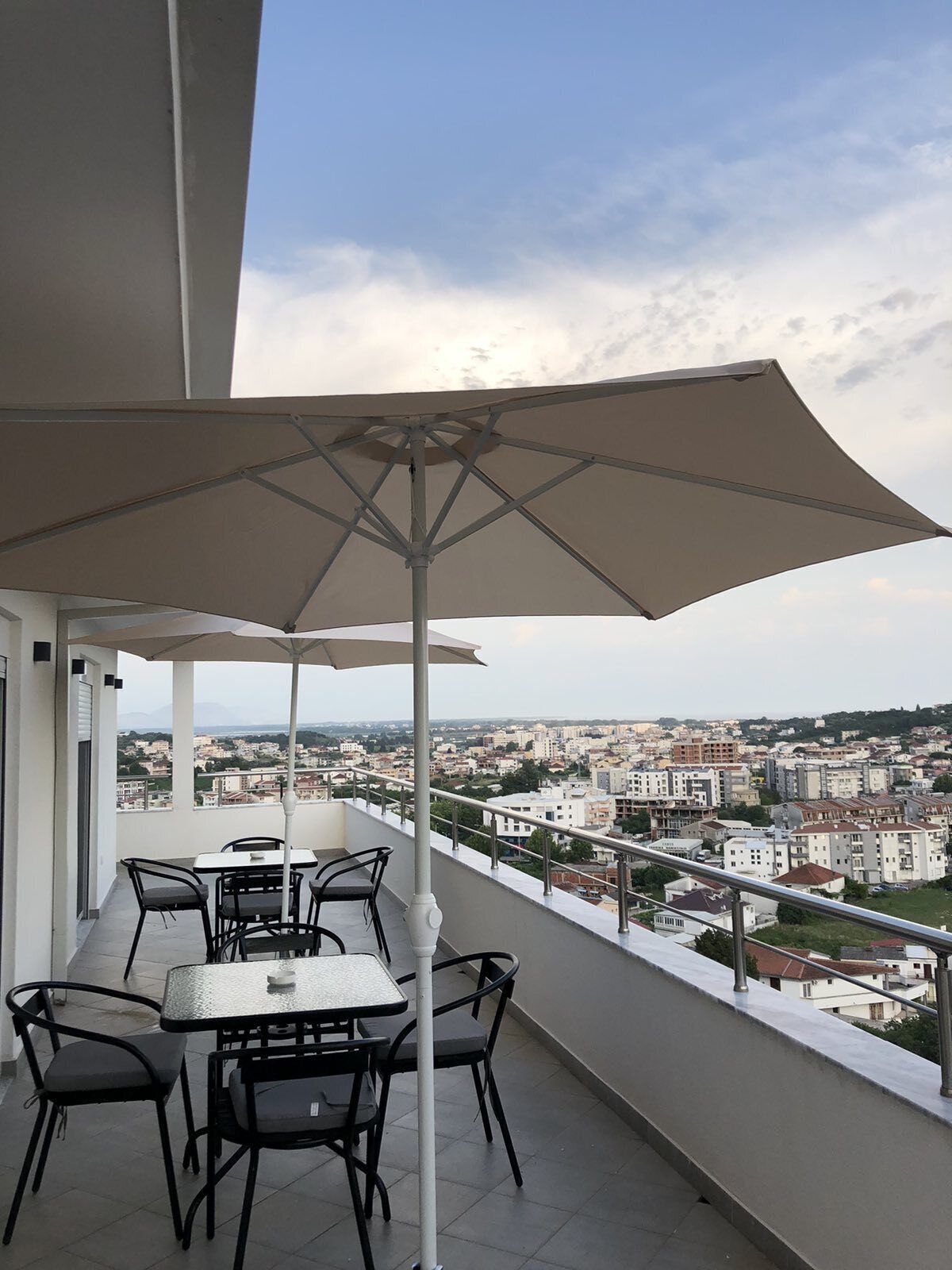 A balcony with a table and chairs, a large umbrella, and a city view.