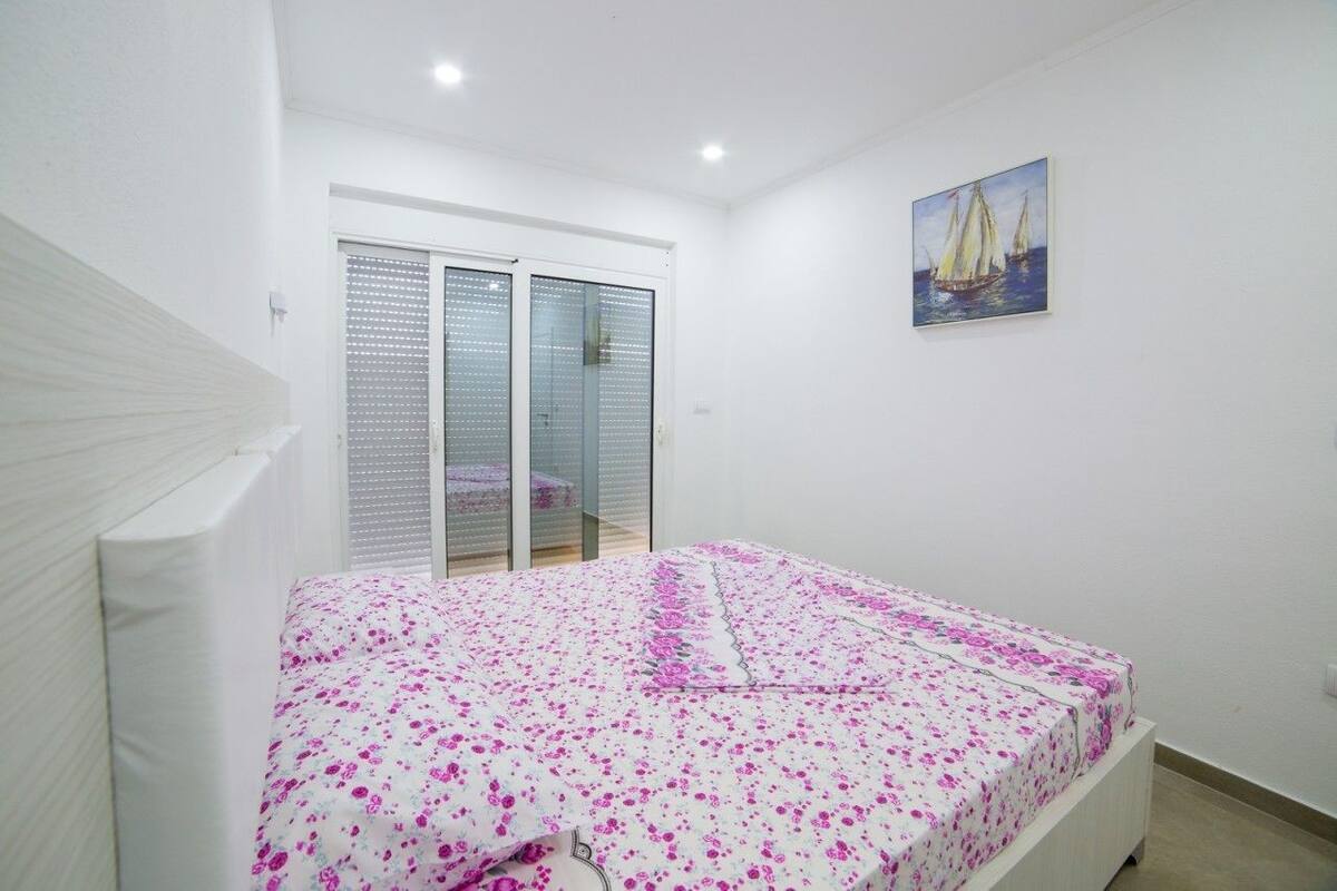 A bedroom with a bed, a sliding glass door, and a painting on the wall.