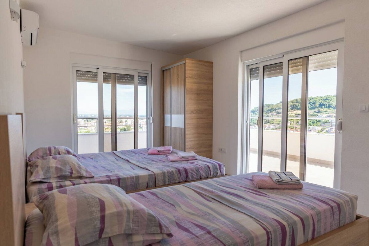 A bedroom with two beds, large windows, and a view of the city.