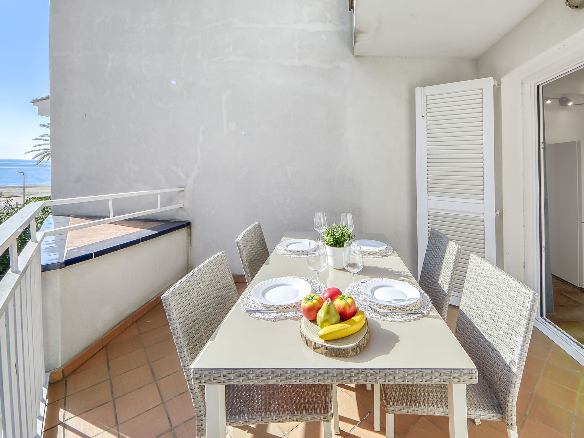 A balcony with a table set for two, featuring a fruit centerpiece, white plates, and clear glasses.