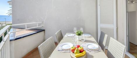 A balcony with a table set for two, featuring a fruit centerpiece, white plates, and clear glasses.