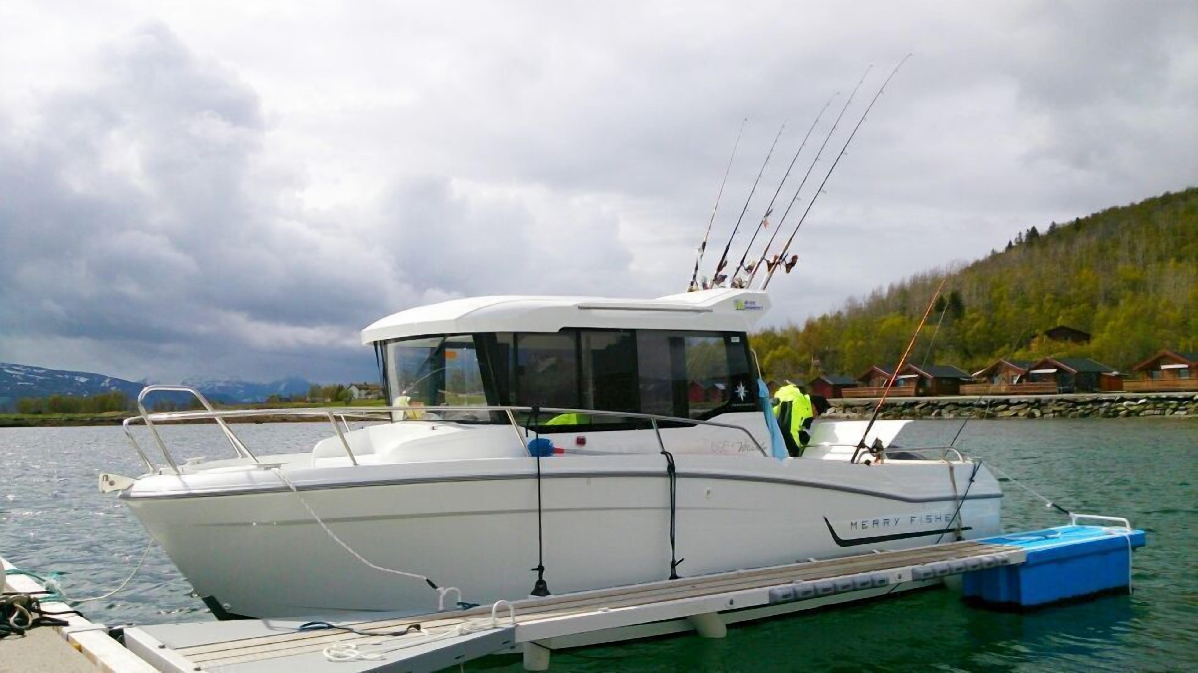 Un barco motor blanco amarrado en un muelle, con cabina, cañas de pescar y un motor fueraborda azul.