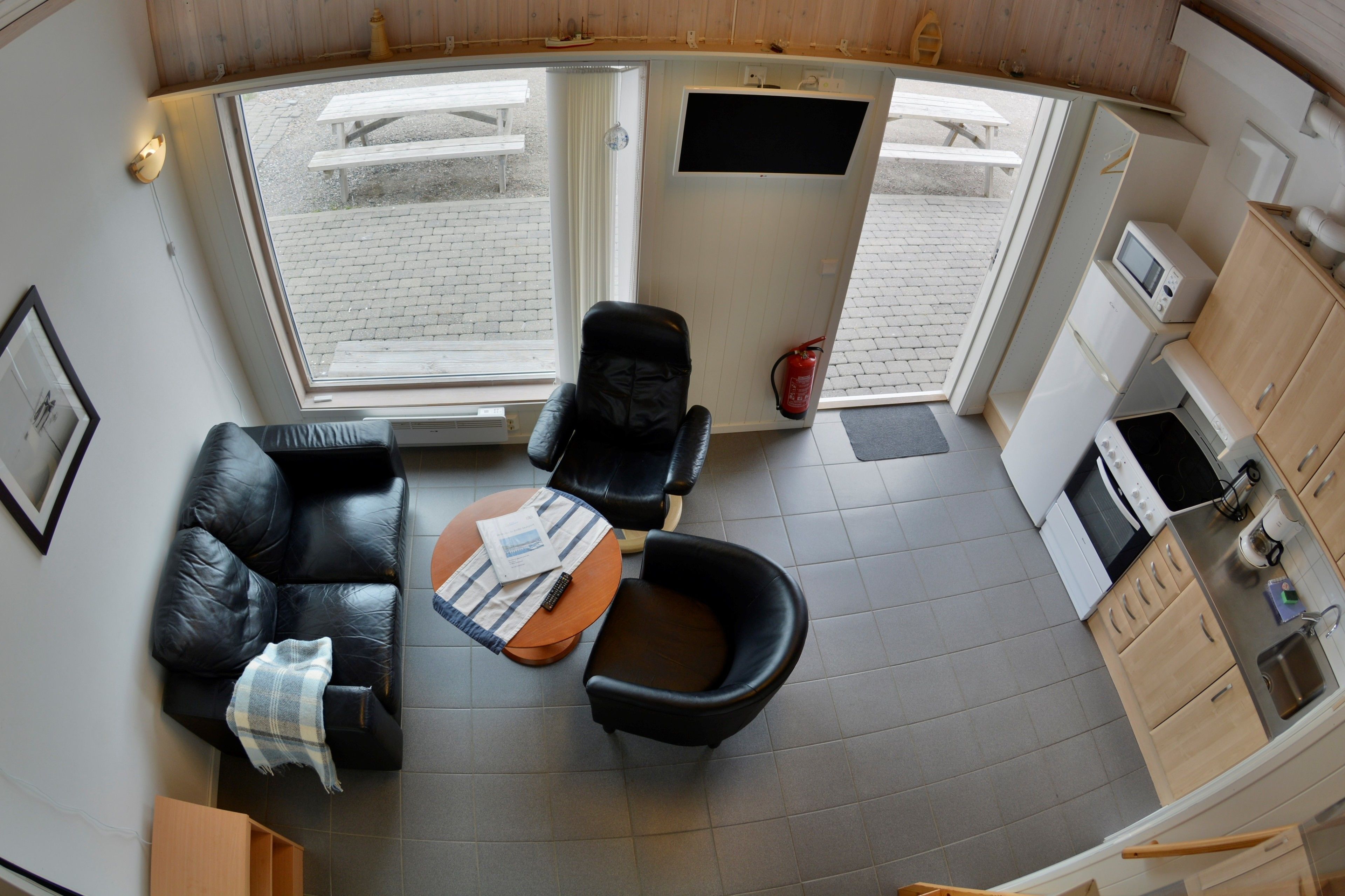 Un espace de vie compact comprenant un coin cuisine, un coin repas avec une table et des chaises, et une grande fenêtre offrant une vue sur l’extérieur.