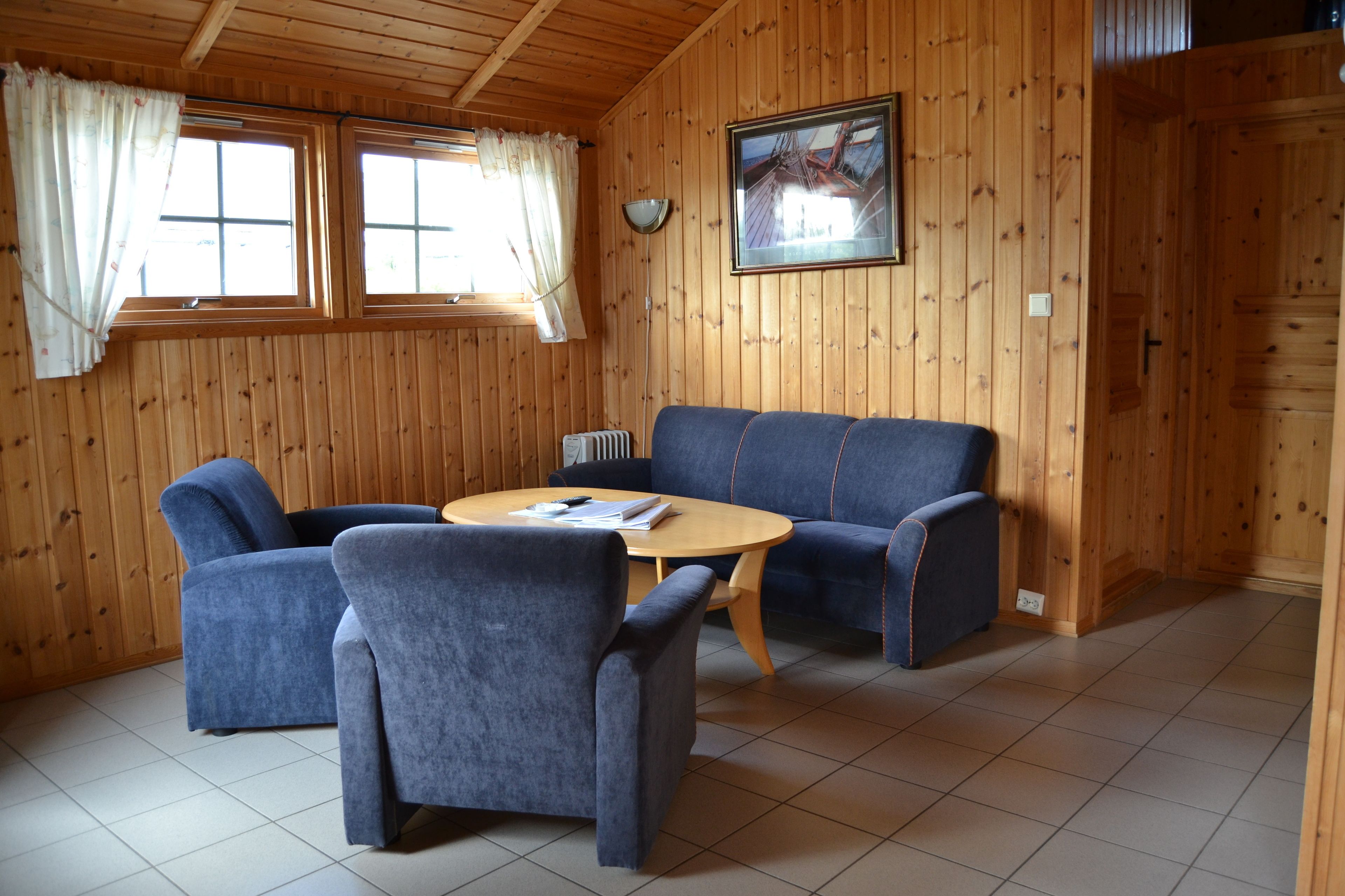 A wooden-paneled room with a blue sofa, two armchairs, and a round wooden table.
