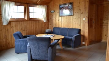 A wooden-paneled room with a blue sofa, two armchairs, and a round wooden table.