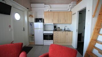 A compact kitchen with white appliances, wooden cabinets, and a red chair.