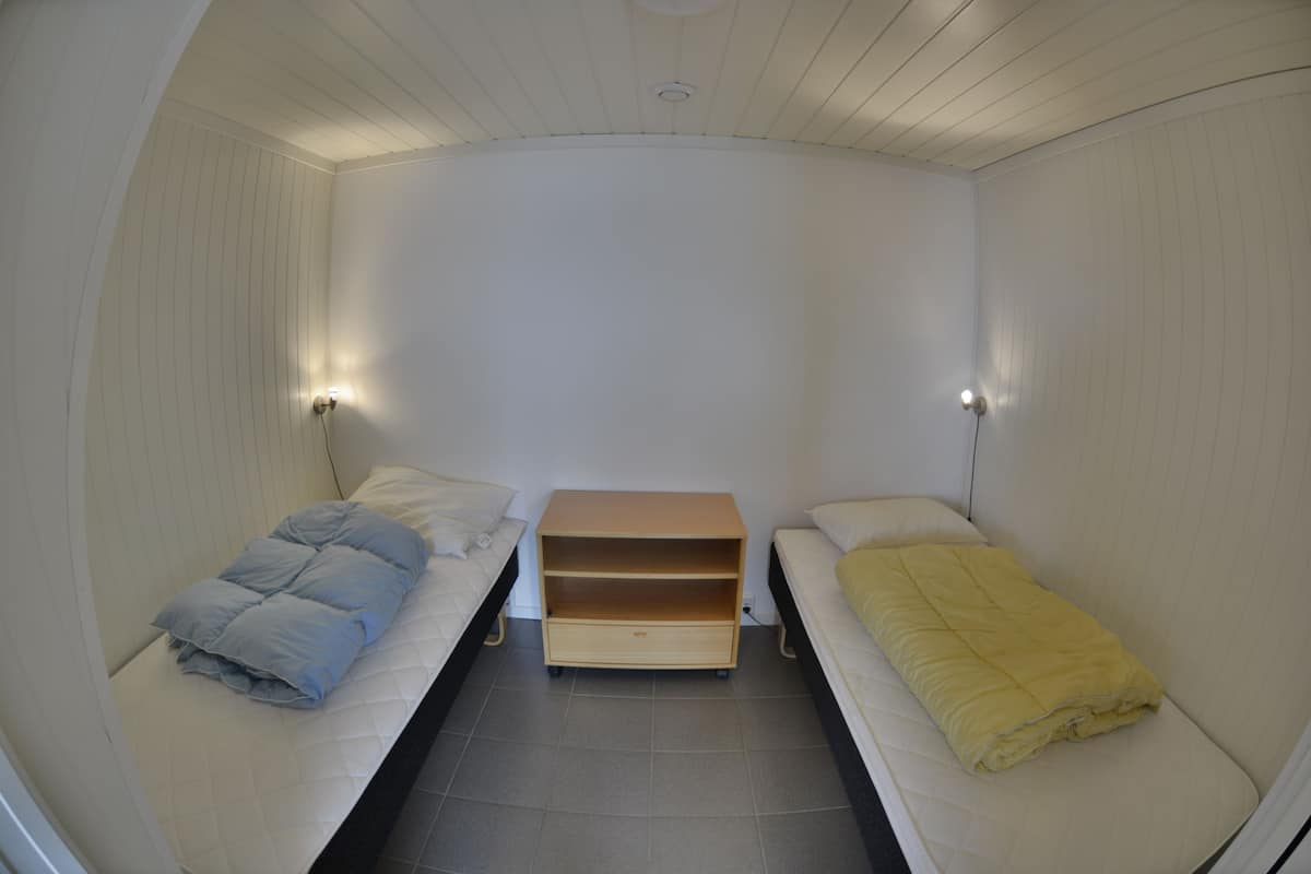 A small, compact room with two single beds, a wooden nightstand, and a wall-mounted light fixture.
