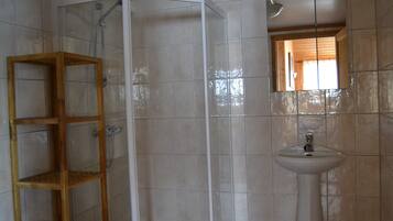 Un baño con cabina de ducha, un estante de madera y un lavabo.