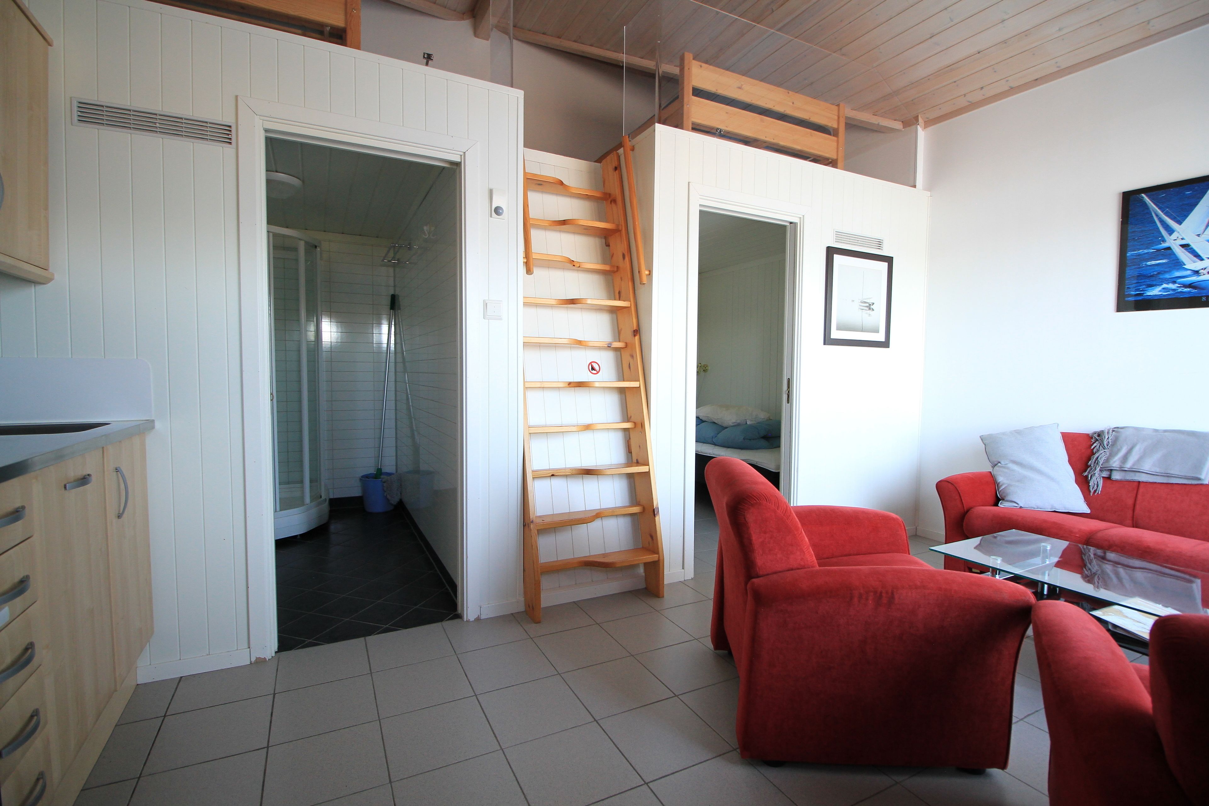 A compact living space with a kitchen area, a red sofa set, a glass coffee table, and a wooden ladder.