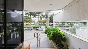 A modern building with large windows, a view of parked cars, and a small garden area with plants. - Vista do Mar, Ótimo Local na Beira-mar Norte (Florianópolis)