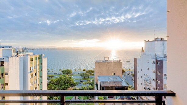 A balcony with a view of a cityscape and a body of water during sunset. - Vista do Mar, Ótimo Local na Beira-mar Norte (Florianópolis)