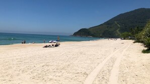 Ein Strand mit blauem Himmel, sandigem Ufer und einem Berg im Hintergrund.