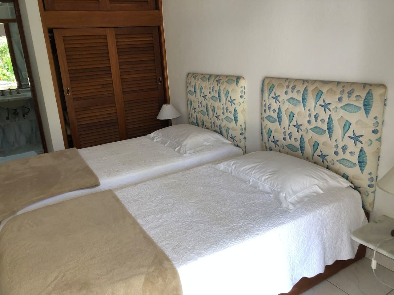 A double bed with a beige blanket, a headboard with a sea-themed pattern, and a bedside table with a lamp.