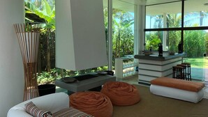 Ein modernes Wohnzimmer mit einer Couch, Sitzsäcken, einem Essbereich mit Bar und großen Fenstern mit Blick auf Grünflächen.