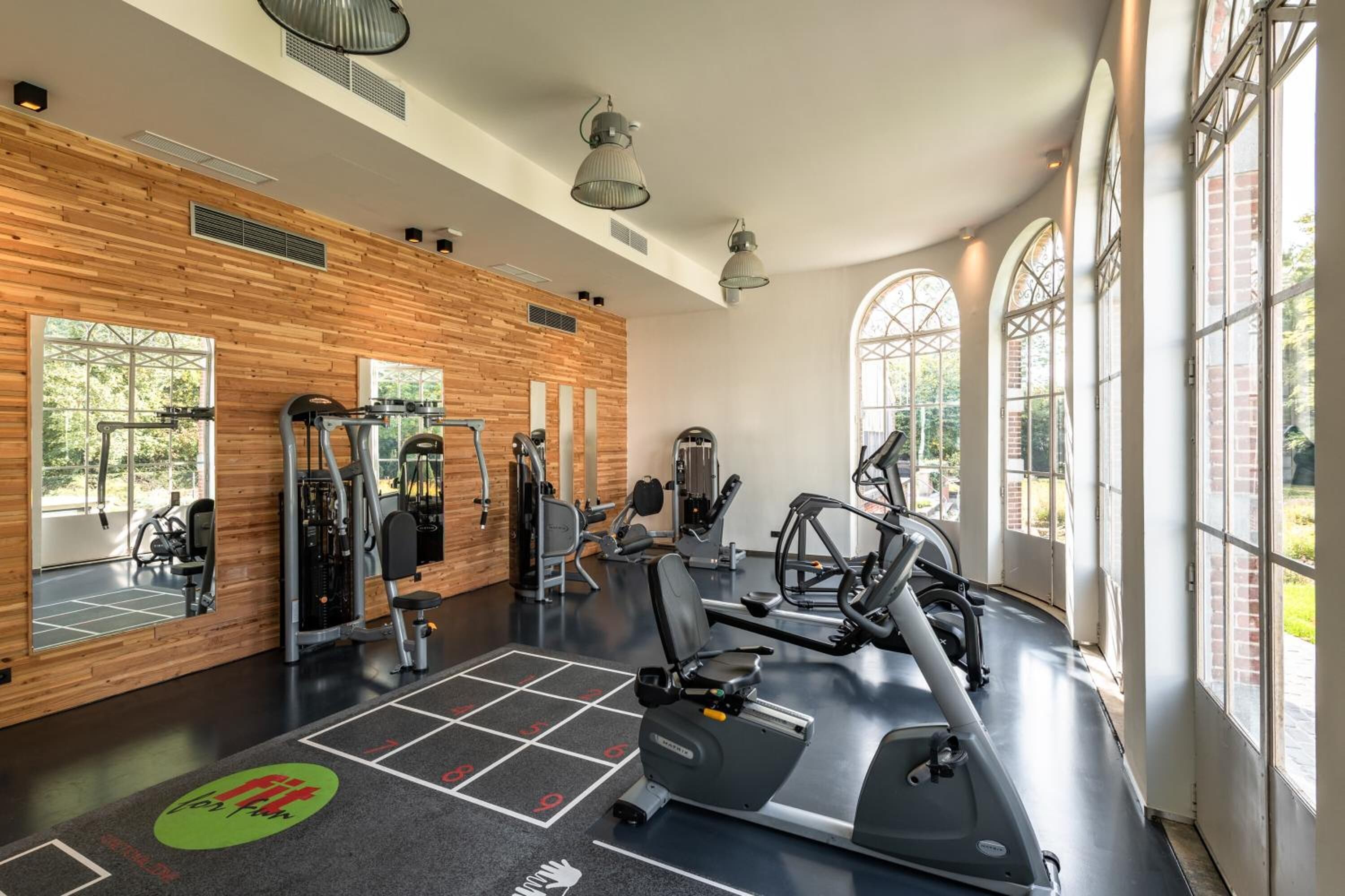 A gym with exercise equipment, large windows, and a wooden wall.