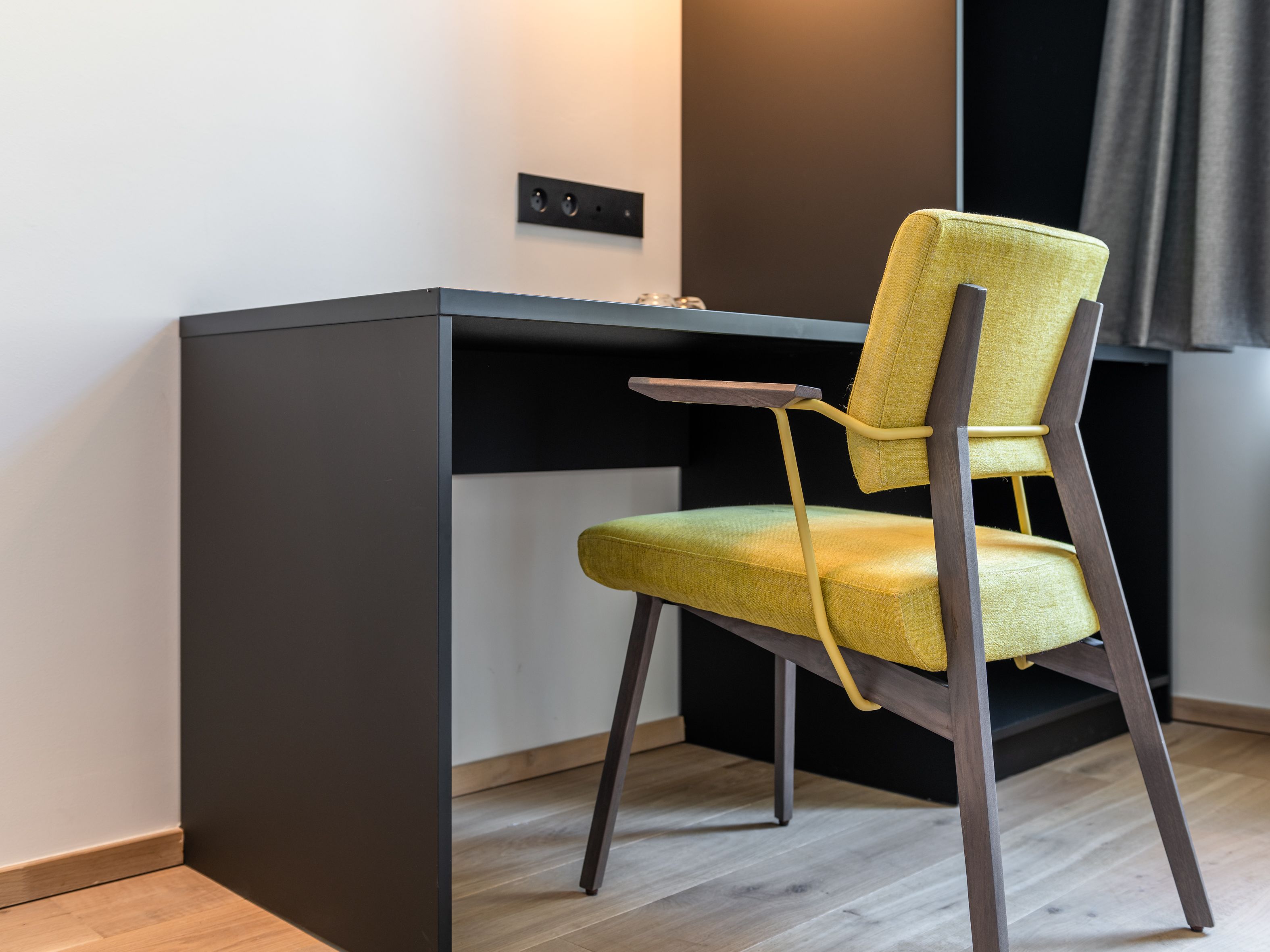 Un espace de travail moderne et compact, doté d’un bureau foncé et d’une chaise jaune.