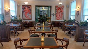 Un restaurant amb taules i caires de fusta, quadres grans a les parets i una escala al fons.