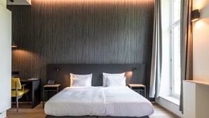 Una habitació d'hotel moderna amb un llit gran, taules de nit, un escriptori i una cadira.