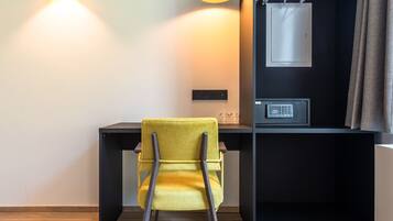 A modern room with a yellow chair, a black desk, a black shelving unit with a safe, and two pendant lights.