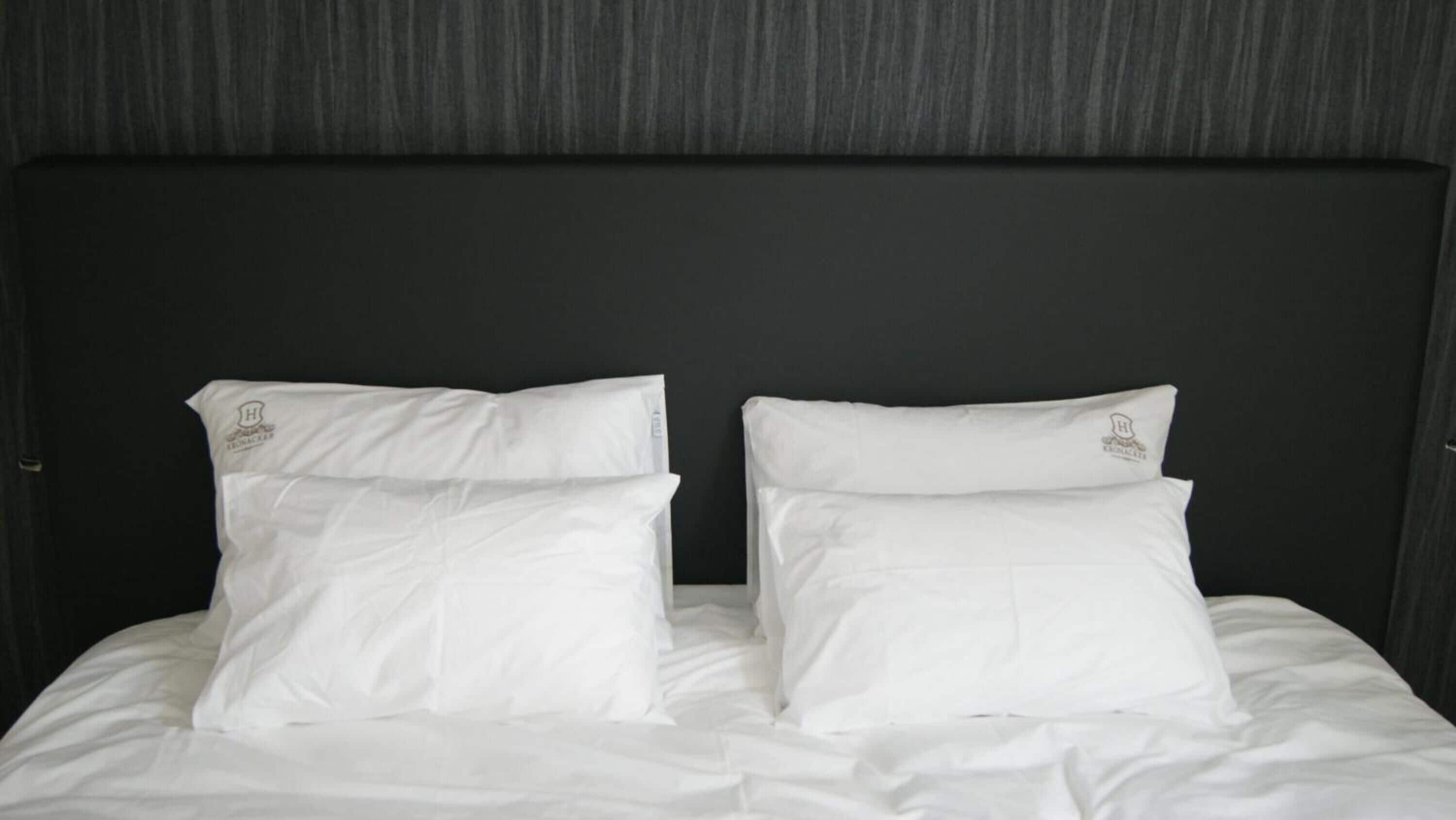Een bed met witte beddengoed en kussens, een donker hoofdeinde en een effen muur.