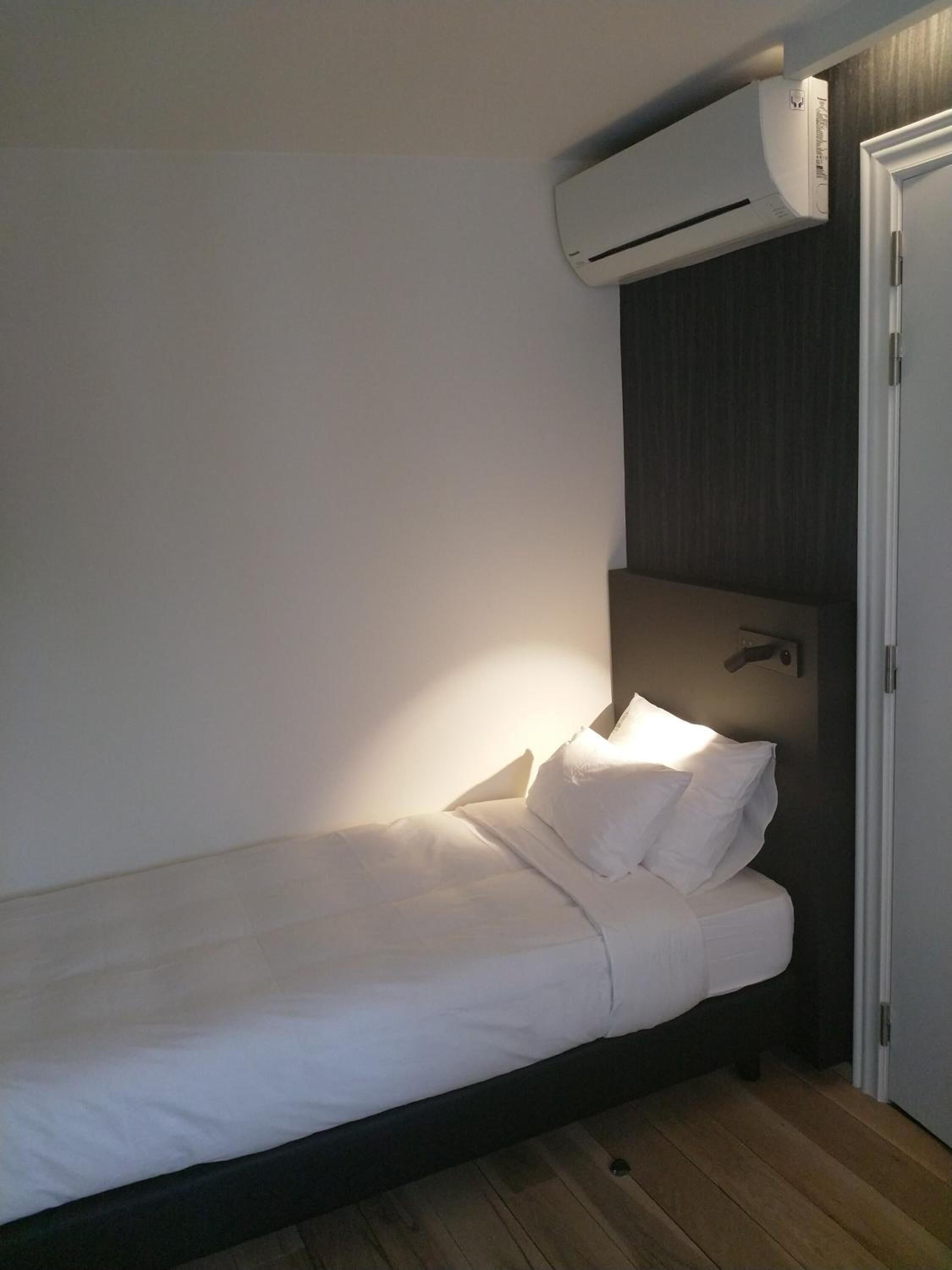 A single bed with white bedding in a room with a dark wooden floor and a white wall.