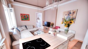 A modern kitchen with a built-in stove, a dining area with a table and chairs, a sofa, and a TV in the background.