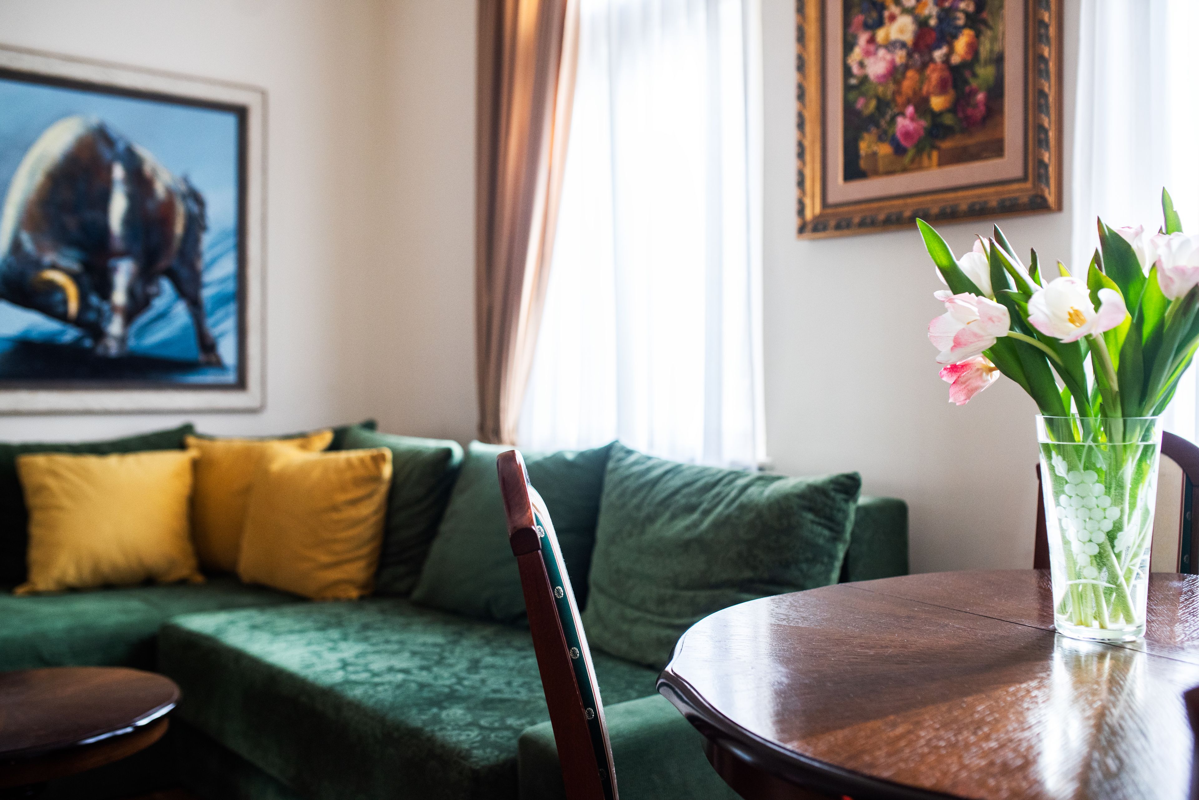 A green sofa with yellow cushions, a wooden table, and a vase with flowers.