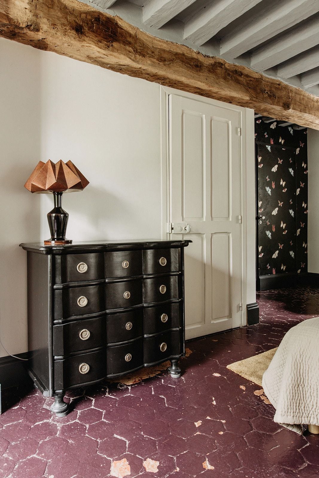 Una habitación con un aparador negro, una puerta blanca y un papel tapiz estampado.