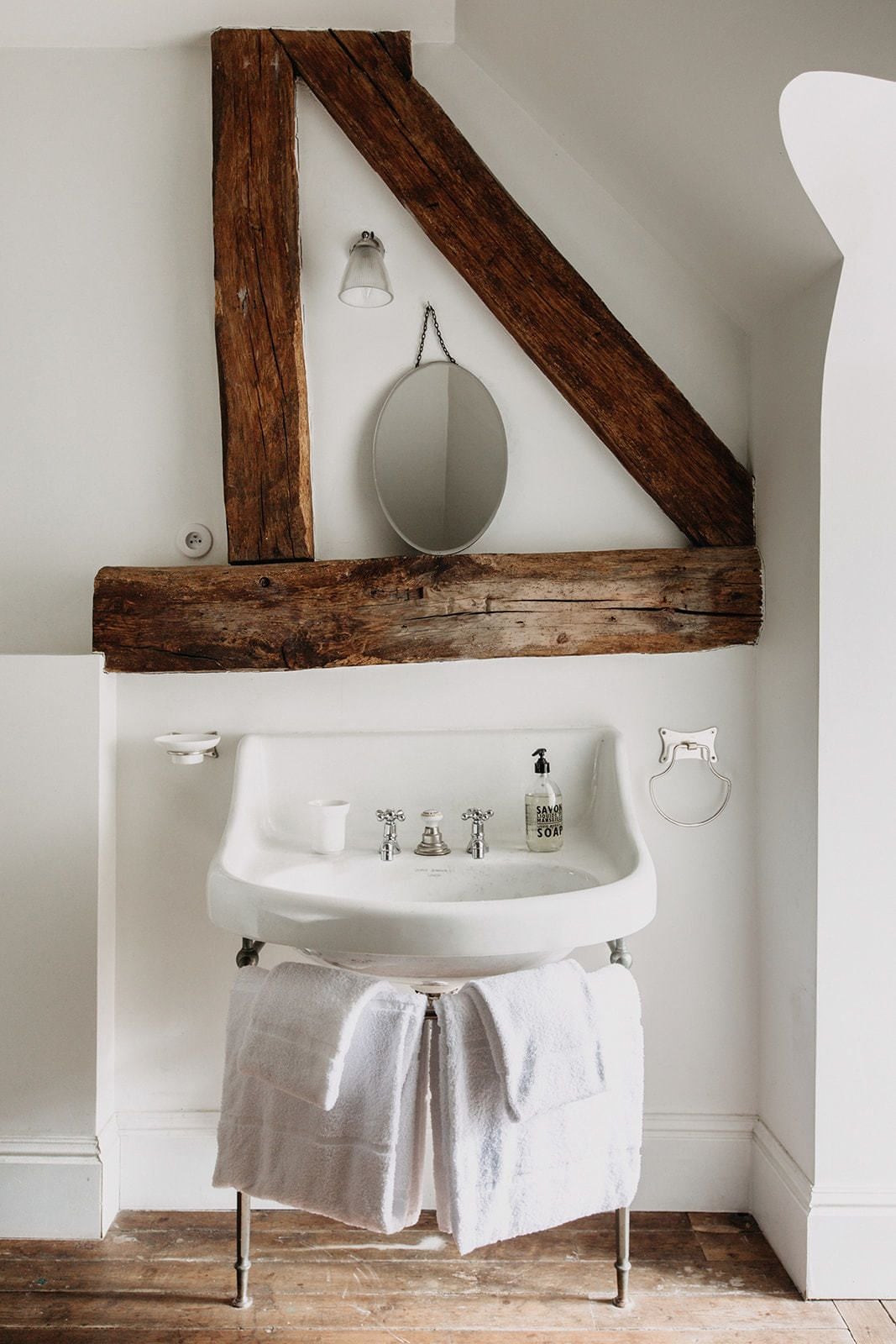 Un baño con lavabo blanco, vigas de madera, un espejo y una toalla colgada en la pared.