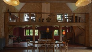 A spacious loft-style room with a high ceiling, exposed wooden beams, and a fireplace. There are multiple seating areas with wooden furniture and large windows providing natural light. - La Dime de Giverny - Chambres D'hôtes (Giverny)
