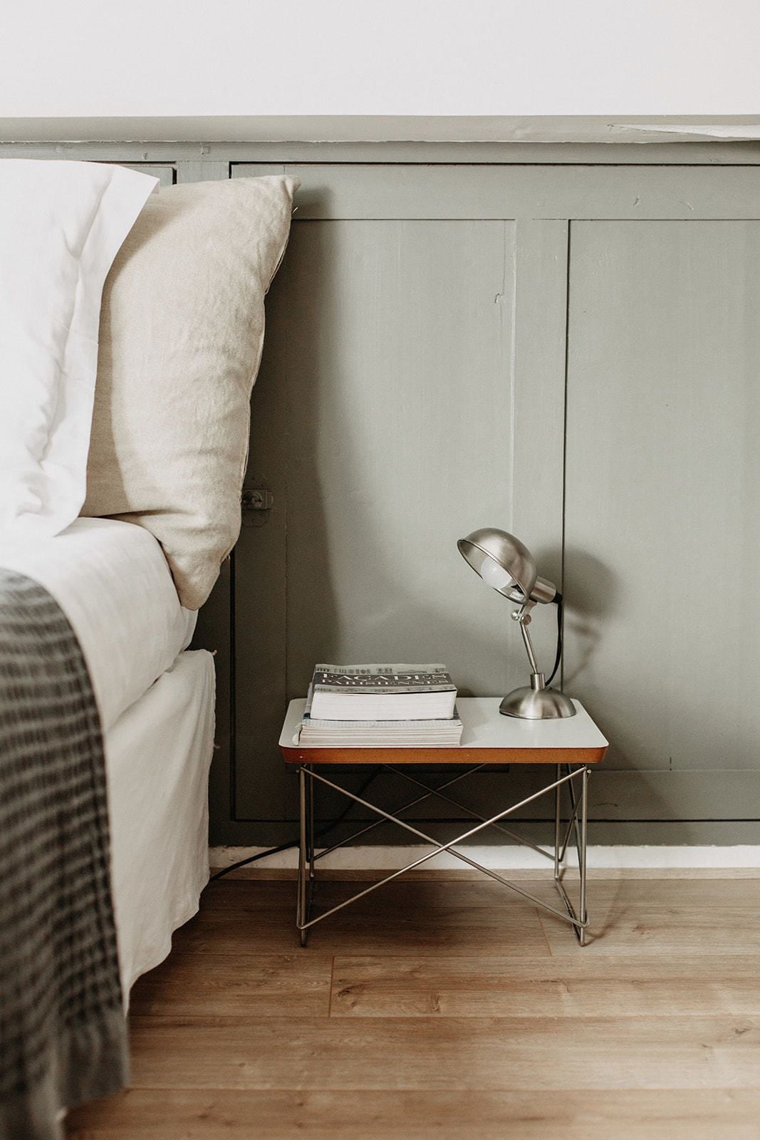 Une chambre à coucher avec un lit, une table de chevet avec des livres et une lampe, et un plancher en bois.
