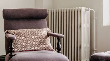 A chair with a patterned cushion and a matching ottoman, placed on a tiled floor with a radiator in the background.