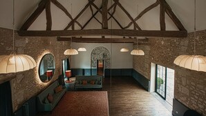 A spacious room with exposed wooden beams, stone walls, and large windows. There is a seating area with a sofa and a table, and pendant lights hanging from the ceiling. - La Dime de Giverny - Chambres D'hôtes (Giverny)